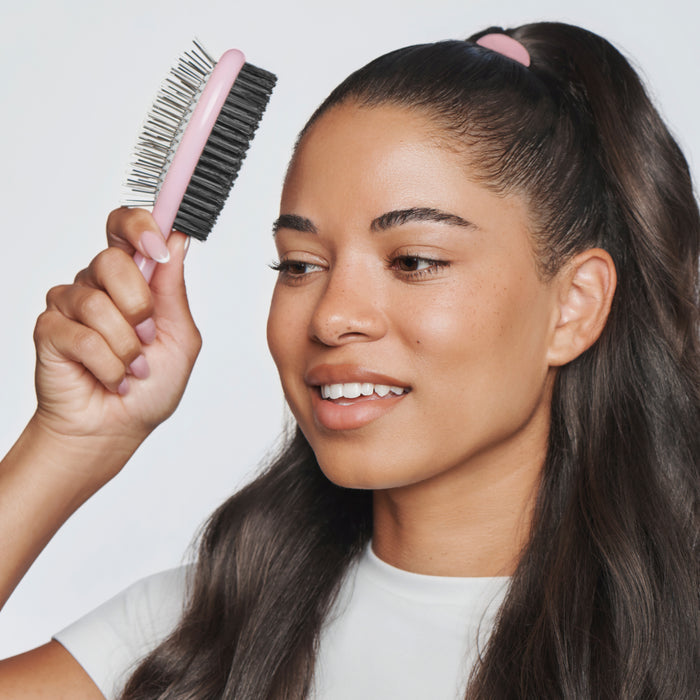 Woman with ponytail holding dual sided brush in front of hair