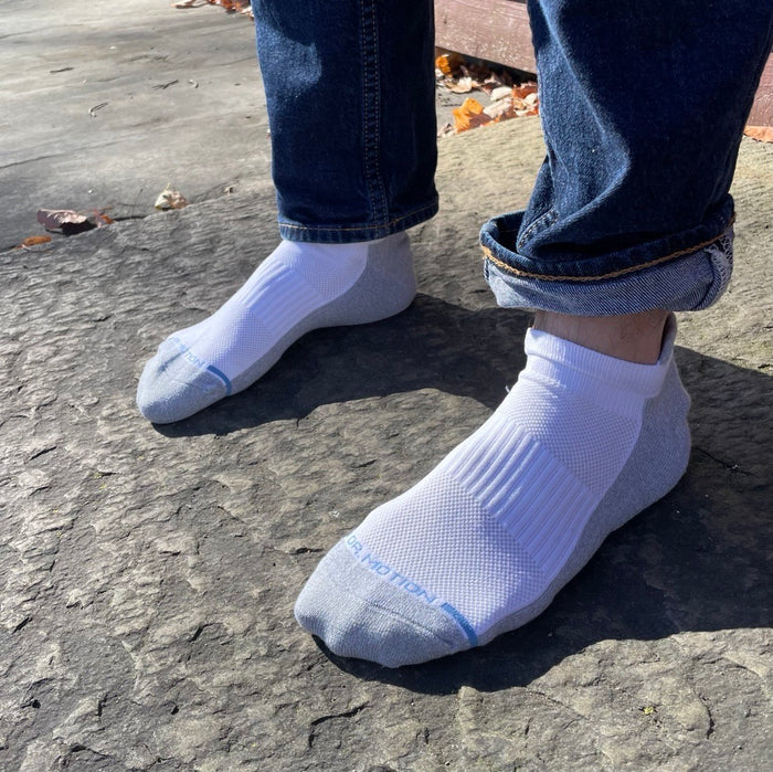 Ankle compression socks in white and gray worn with rolled-up denim jeans on a stone surface.