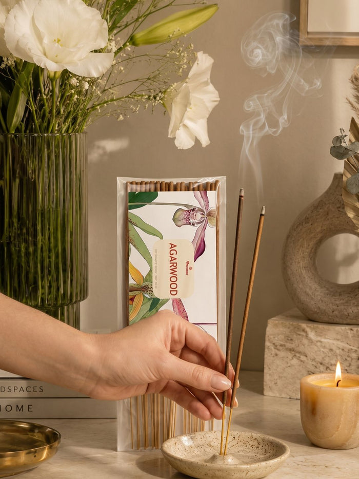 Agarwood incense sticks pack held near a burner, with incense smoke rising