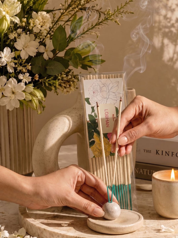 Incense sticks in a stone holder with smoke, held near a prayer flame
