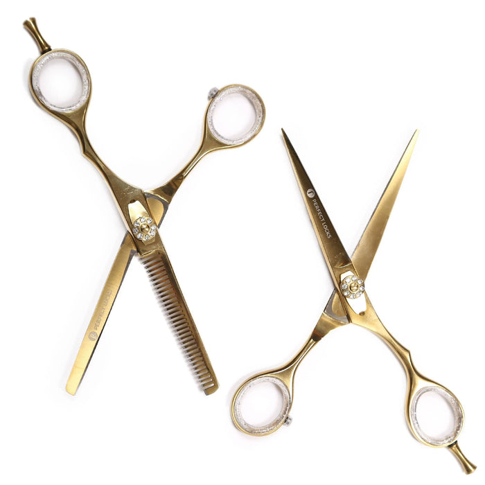 Two gold-colored hairdressing scissors, one straight and one thinning, lie on a white background with finger rests and decorative screws.