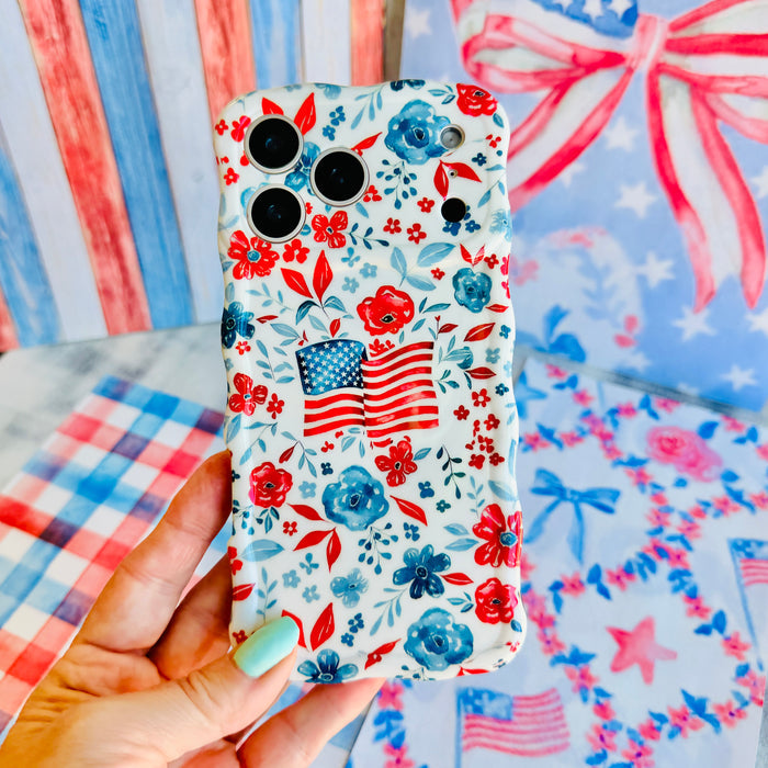 Trendy wavy iPhone case featuring an American flag illustration surrounded by a red and blue watercolor floral pattern with a high-gloss finish.