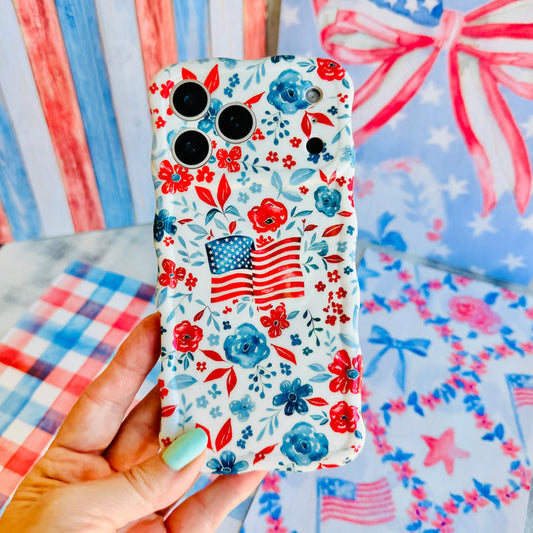 Trendy wavy iPhone case featuring an American flag illustration surrounded by a red and blue watercolor floral pattern with a high-gloss finish.