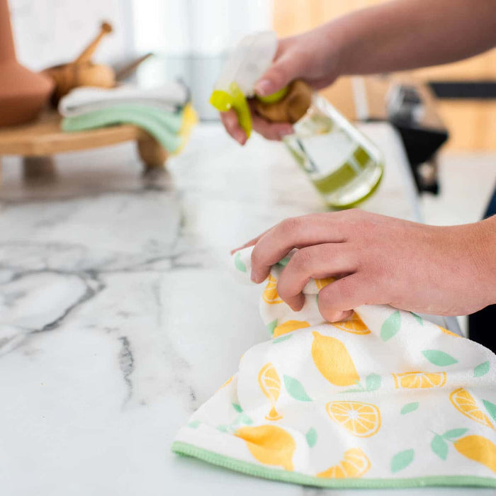 Person holding a colorful kitchen towel with lemon pattern on a marble countertop.
