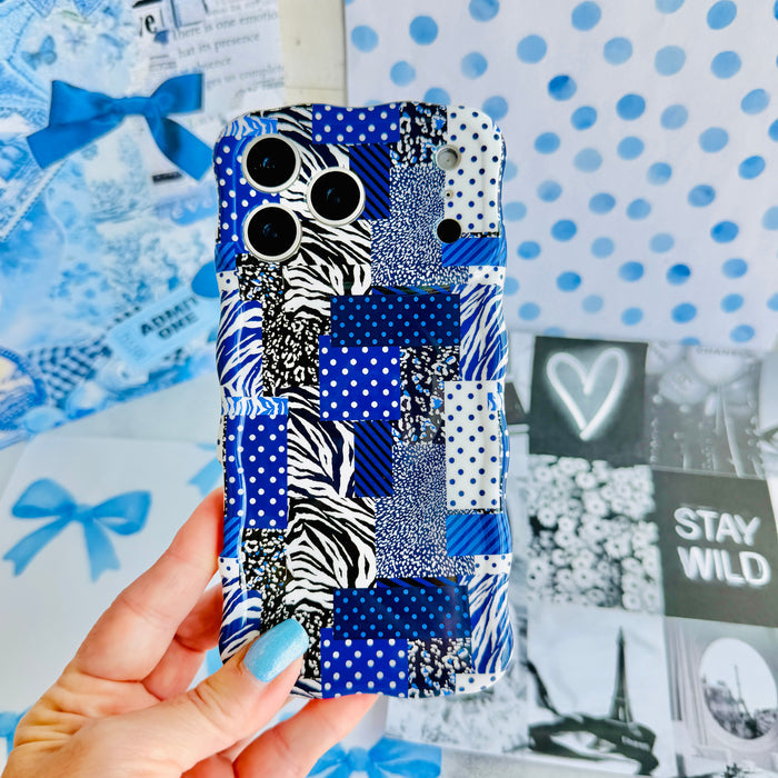 Hand holding the Sending Mixed Signals Wavy Luxe MagSafe iPhone case, showing the blue patchwork print mixing gingham, polka dots, zebra stripe and florals.