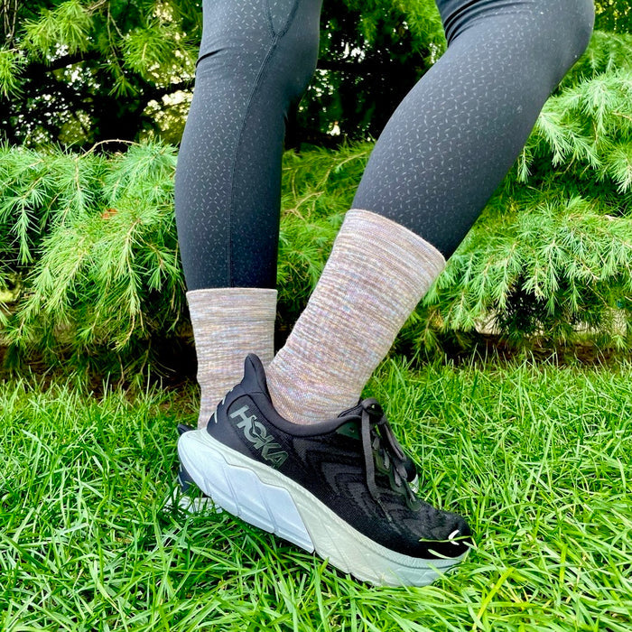 Black athletic shoes with white soles, paired with medium-weight, spacedye crew socks and black leggings, on grass.