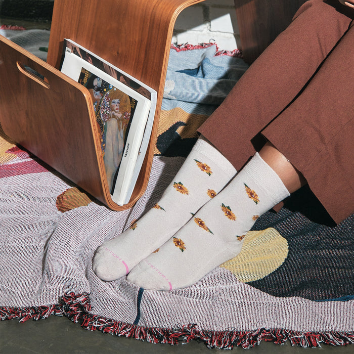 Light gray socks with sunflower patterns, worn by a person seated on a colorful woven rug.
