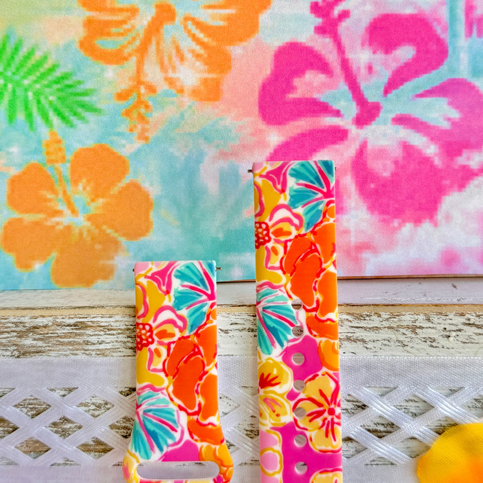 Sunset Hibiscus silicone Samsung Watch band with vibrant pink, orange, yellow, and teal tropical hibiscus floral print, shown displayed and worn on Apple Watch against a colorful tropical floral backdrop.