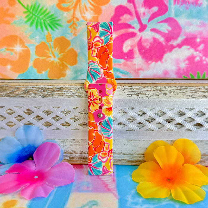 Sunset Hibiscus silicone Samsung Watch band with vibrant pink, orange, yellow, and teal tropical hibiscus floral print, shown displayed and worn on Apple Watch against a colorful tropical floral backdrop.