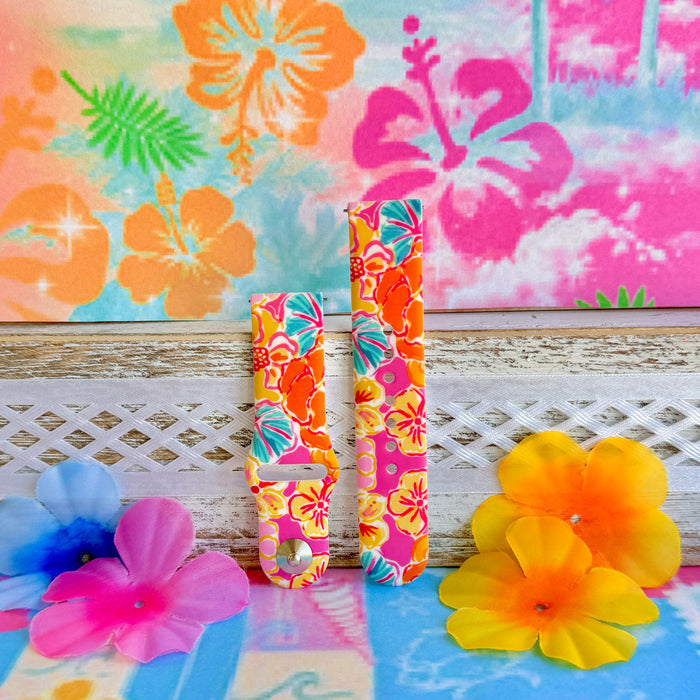 Sunset Hibiscus silicone Samsung Watch band with vibrant pink, orange, yellow, and teal tropical hibiscus floral print, shown displayed and worn on Apple Watch against a colorful tropical floral backdrop.