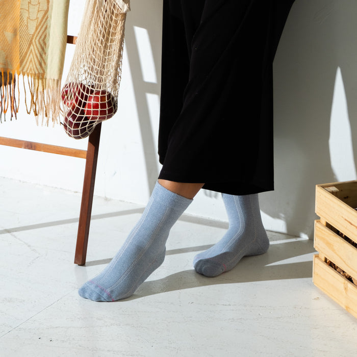 Light blue half-cushion socks with a textured pattern, worn with black pants, against a minimalist background.