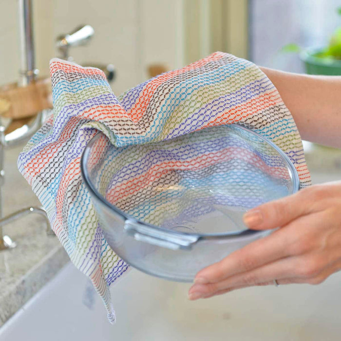 A close-up of a person holding a clear glass bowl and using a multicolour striped tidy dish cloth from Full Circle for drying.