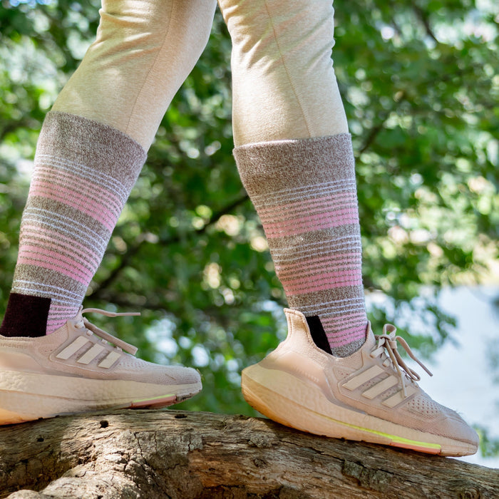 Medium weight crew socks with a striped pattern in pink and brown, worn with light athletic shoes on a tree branch.